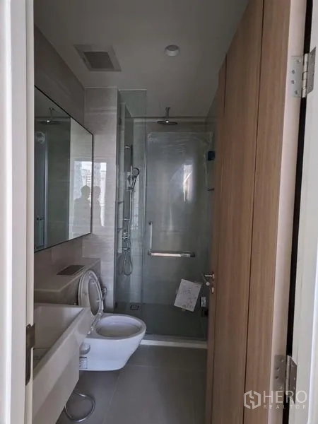 Condominium for sale - Compact bathroom featuring a glass-enclosed rain shower, toilet, and vanity.