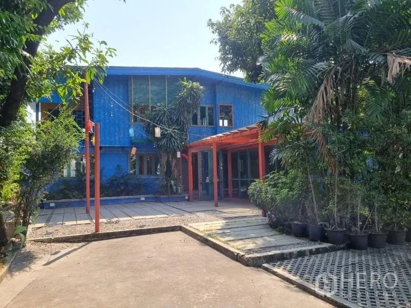 Detached House for rent in Khlong Toei, Bangkok - Front view of a blue two-storey detached house with red pergola, trees and driveway in Ekkamai.