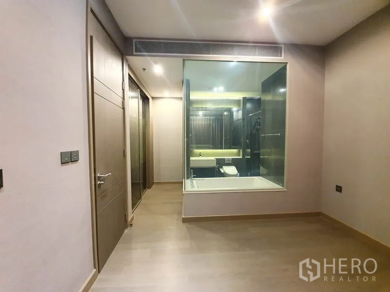 Condominium for rent in Huai Khwang, Bangkok - Bedroom view toward the bathroom through a large glass panel, wood flooring, and recessed lights.