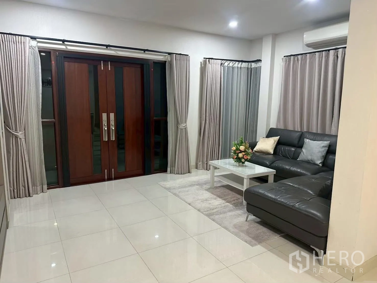 独栋房屋 for rent in Bang Phli, Samut Prakan - 明亮客厅有L形皮沙发、茶几和木质双扇门。