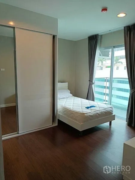 Condominium for rent or sale in Huai Khwang, Bangkok - Bedroom with sliding wardrobe and balcony accessed through glass doors.