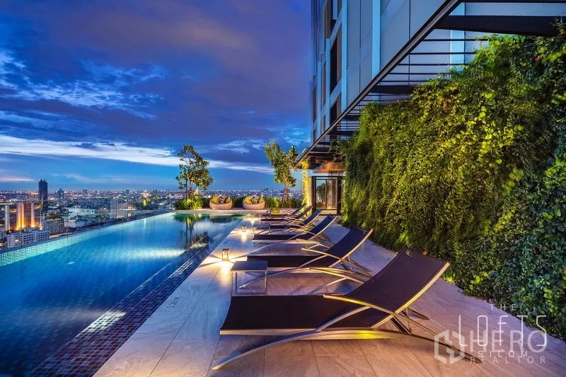 公寓 出租在Bang Rak, Bangkok - 屋顶无边际泳池，躺椅与垂直绿墙，远眺城市。