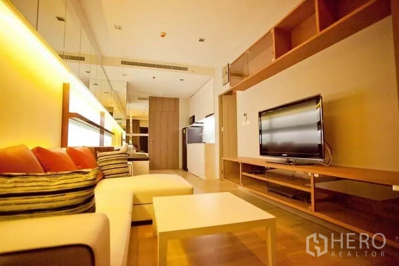 Condominium for rent or sale in Watthana, Bangkok - Cozy lounge area with sectional sofa, warm lighting and wall-mounted TV unit.