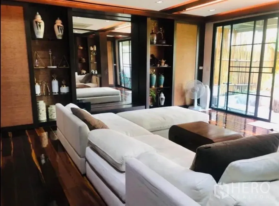 Condominium for rent in Pathum Wan, Bangkok - Bright living room with white sectional sofa, built‑in display shelves, polished hardwood floors and sliding glass doors.