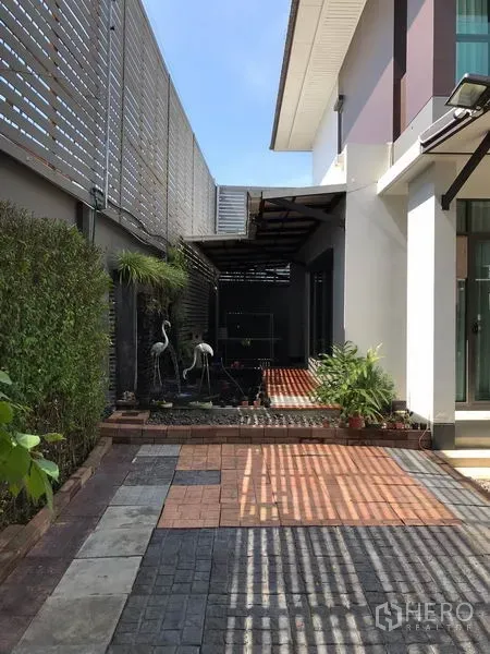 独立式住宅 出租在Bang Kapi, Bangkok - 房屋侧院铺砖露台与景观水池，周围是修剪整齐的灌木。
