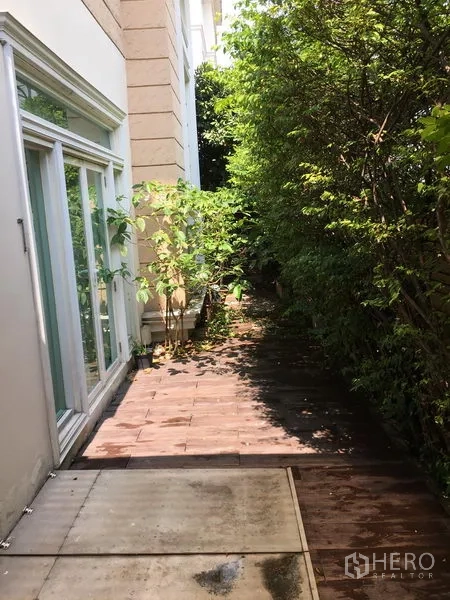 ทาวน์เฮาส์ ขายในHuai Khwang, Bangkok - ทางเดินสวนข้างบ้านร่มรื่น ประตูกระจกบานเลื่อน และต้นไม้หนาแน่น