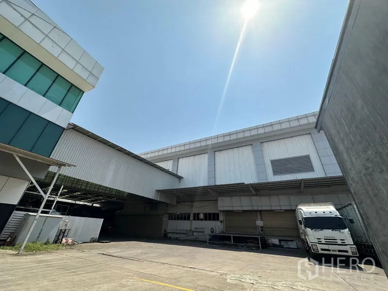 Warehouse for rent in Lam Luk Ka, Pathum Thani - Modern warehouse exterior with covered loading bays and a parked truck under a bright sky.