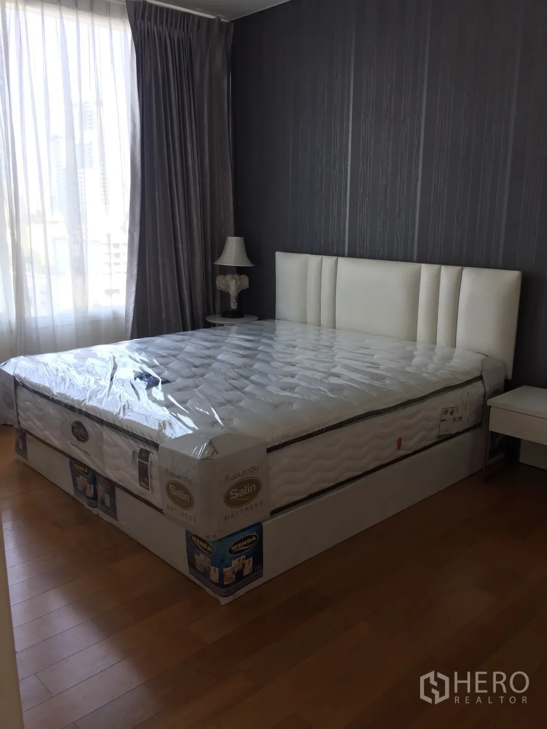 คอนโด ให้เช่าในWatthana, Bangkok - ห้องนอนพร้อมเตียงควีน เฮดบอร์ดบุหนังสีขาว ผนังลายเทา และหน้าต่างบานใหญ่พร้อมผ้าม่าน