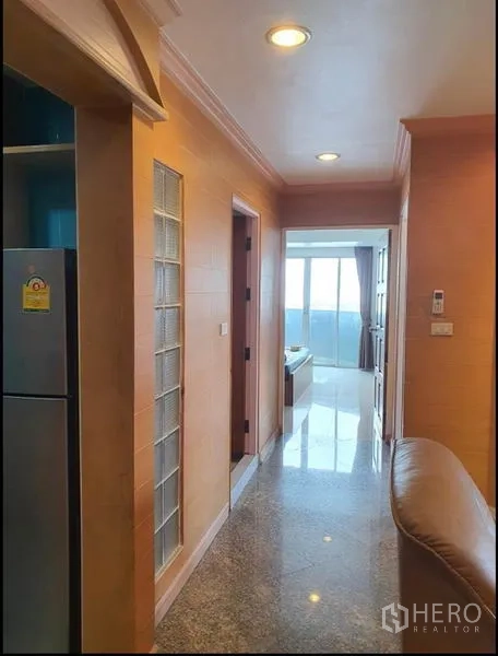 Condominium for rent in Ratchathewi, Bangkok - Hallway with recessed lights leading to a bright room and polished stone floor.