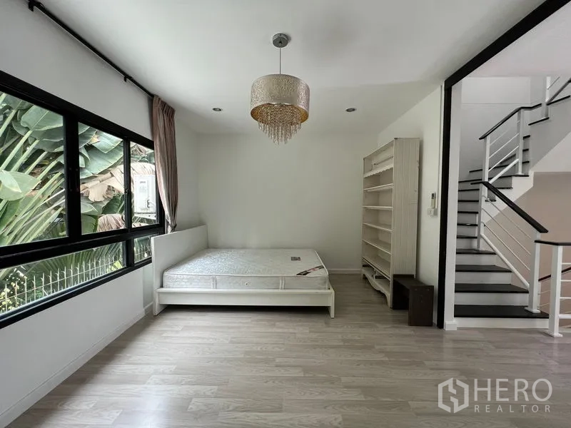 ทาวน์เฮาส์ ขายในBang Kapi, Bangkok - ห้องนอนชั้นล่างพร้อมเตียง ชั้นวาง และหน้าต่างบานใหญ่ข้างบันได