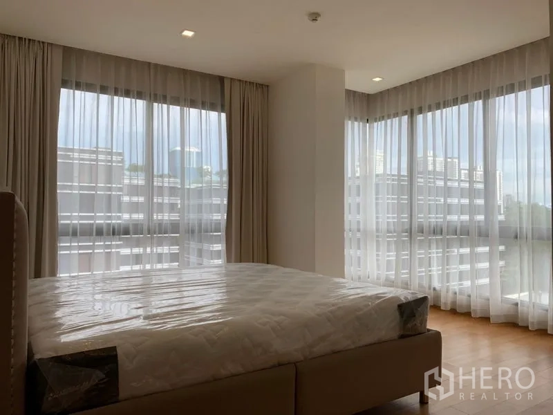 Condominium for sale in Khlong Toei, Bangkok - Corner bedroom with wraparound floor-to-ceiling windows and urban outlook.