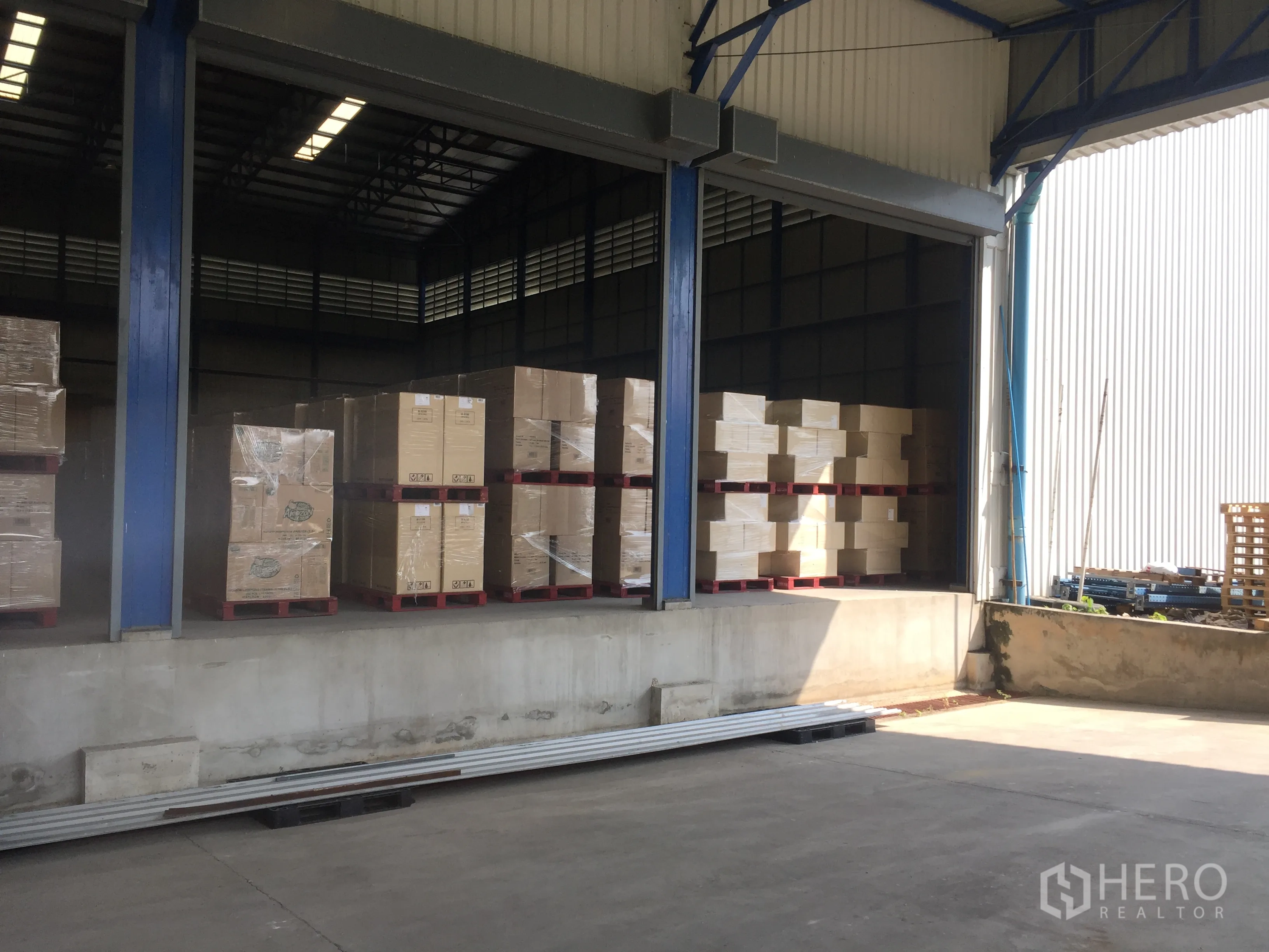 Warehouse for rent in Pak Kret, Nonthaburi - Sheltered loading bay with stacked pallets and boxed goods under a high roof.