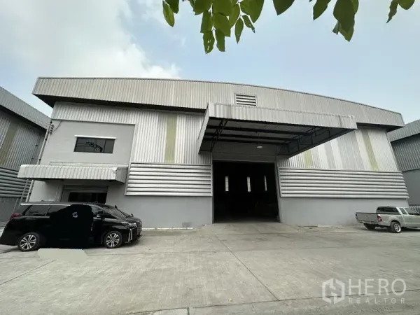 货栈 出租在Bang Phli, Samut Prakan - 仓库正面，大型卷帘门入口，侧边连接办公室并设有雨棚。