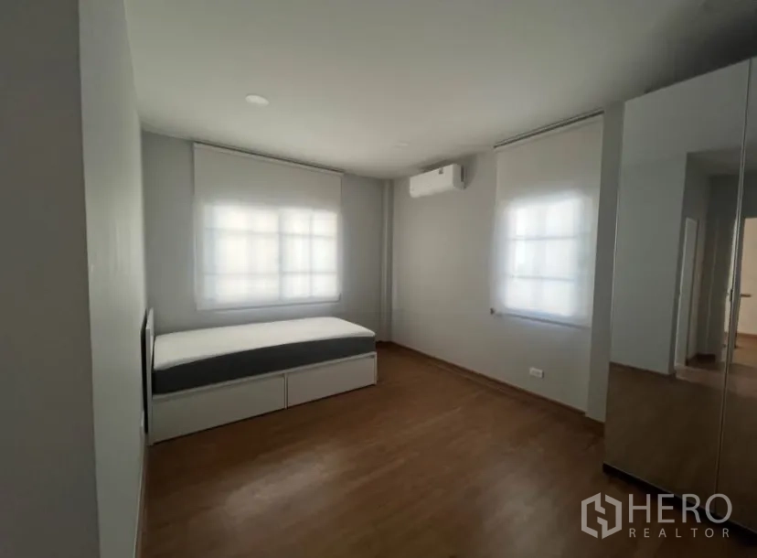 Detached House for rent in Bang Phli, Samut Prakan - Minimal guest bedroom with single bed, air conditioner, two bright windows, wood flooring and wardrobe mirror.