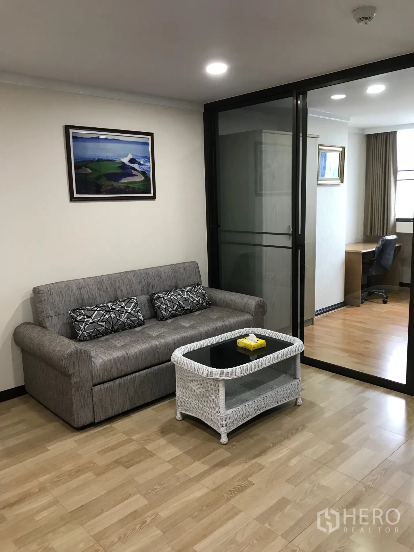 公寓 出租或出售在Watthana, Bangkok - 客厅配灰色沙发与玻璃台藤编茶几，木地板与玻璃推拉门