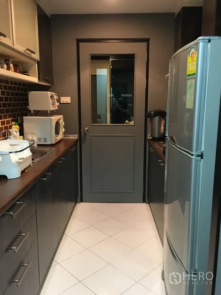 公寓 出售在Khlong Toei, Bangkok - 独立走廊式厨房，深色橱柜、全套家电与大冰箱。