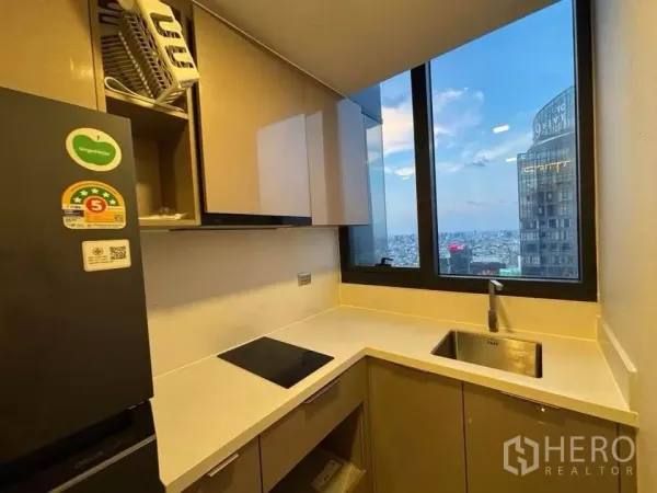 公寓 出租在Huai Khwang, Bangkok - 紧凑厨房，内置橱柜、电磁炉与大窗城市景观。