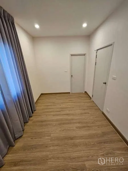 Detached House for rent in Bang Phli, Samut Prakan - Compact room with wood flooring, two internal doors and tall curtains.