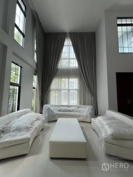 Detached House for rent or sale in Prawet, Bangkok - Double-height living room with tall curtains and three white sofas wrapped for move-in.