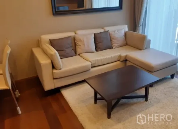 คอนโด ให้เช่าในWatthana, Bangkok - ห้องนั่งเล่นอบอุ่นด้วยโซฟาเข้ามุมสีเบจ โต๊ะกลาง พรม และกระจกเงาบนผนัง