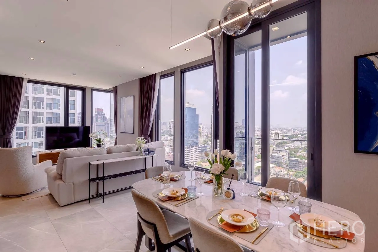 Condominium for rent or sale in Watthana, Bangkok - Open-plan living and dining area with a marble table, modern pendant lighting, and floor-to-ceiling windows overlooking the city skyline.