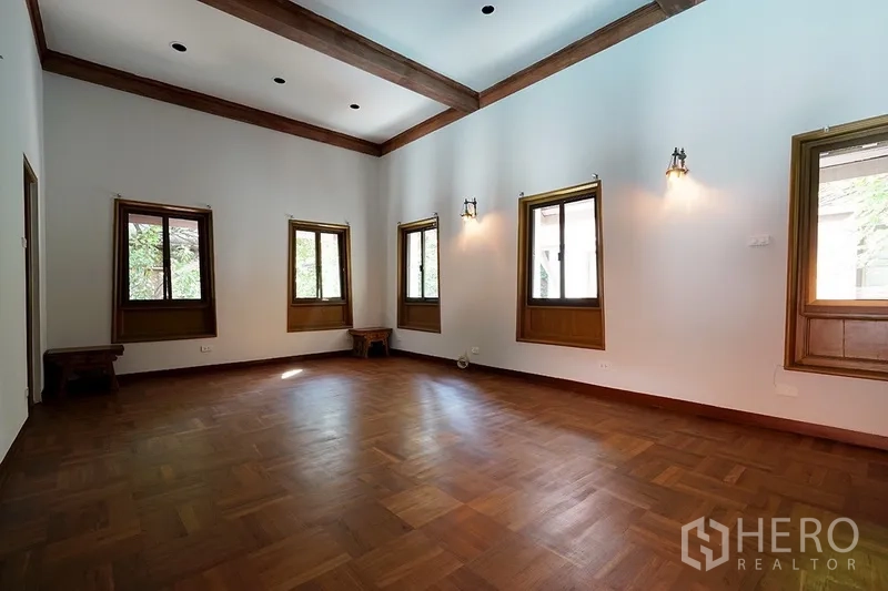 บ้าน ให้เช่าในWatthana, Bangkok - ห้องนั่งเล่นกว้างพื้นปาร์เกต์ เพดานสูงคานไม้ และหน้าต่างกรอบไม้หลายบาน