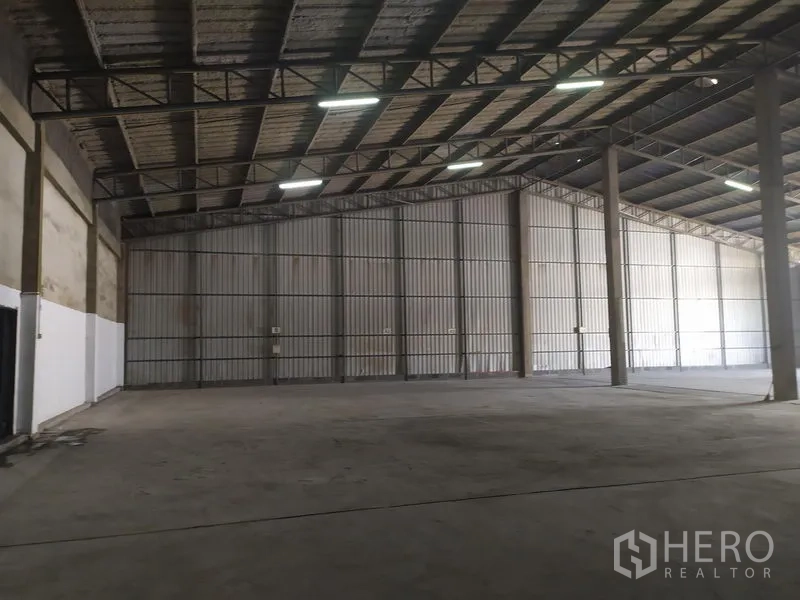 Warehouse for rent in Samut Prakan - Spacious warehouse interior with high steel truss roof, ample lighting and smooth concrete floor.