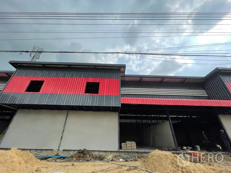 货栈 出租在Pathum Thani - 低角度外观，屋檐、空中电线与红色立面板。