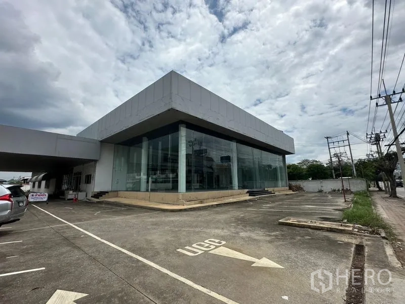 Showroom for rent or sale in Lam Luk Ka, Pathum Thani - Glass-front corner showroom building with wide forecourt parking.
