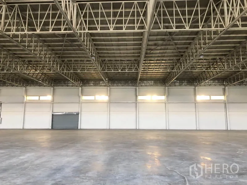 Warehouse for rent in Bang Sao Thong, Samut Prakan - High-bay wall with windows and a closed roller shutter inside the warehouse.