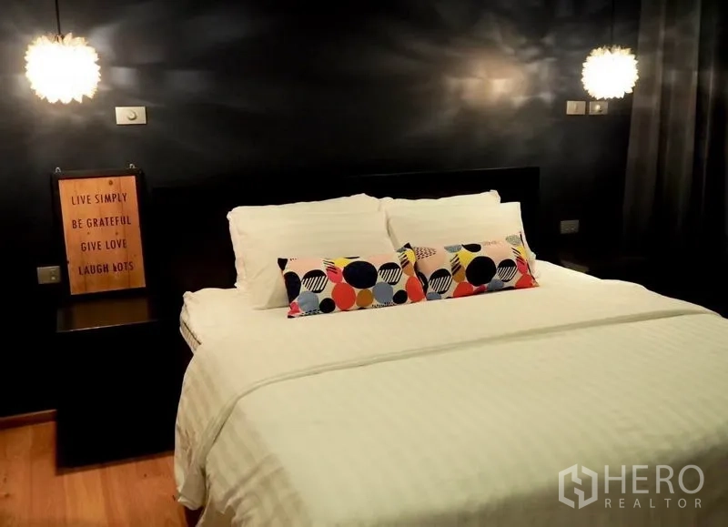 คอนโด ให้เช่าในWatthana, Bangkok - ห้องนอนบรรยากาศสงบ เตียงคิงไซส์ ผนังสีเข้ม โคมไฟห้อย และหมอนลายสีสัน