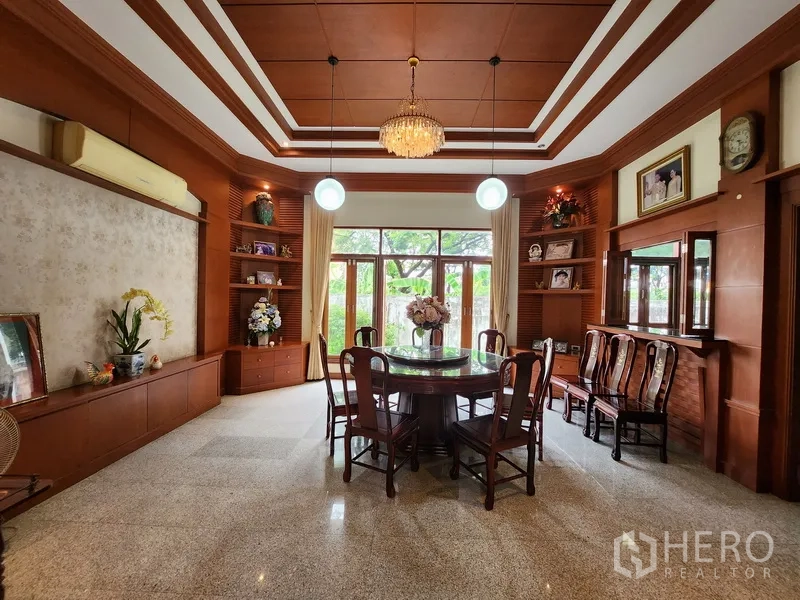 独立式住宅 出租在Prawet, Bangkok - 正式餐厅，格栅吊顶与木质壁柜，圆桌面向庭院窗景。