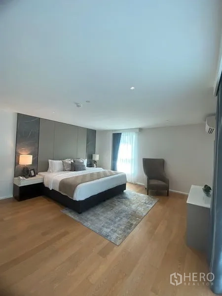 Condominium for rent in Watthana, Bangkok - Spacious master bedroom with king bed, wood floors, accent wall, and large window.