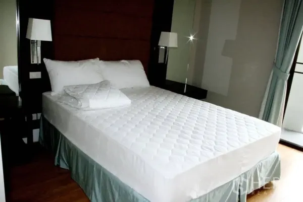 公寓 出租或出售在Watthana, Bangkok - 明亮卧室，双人床、软包床头、床侧灯与通往阳台的推拉门。