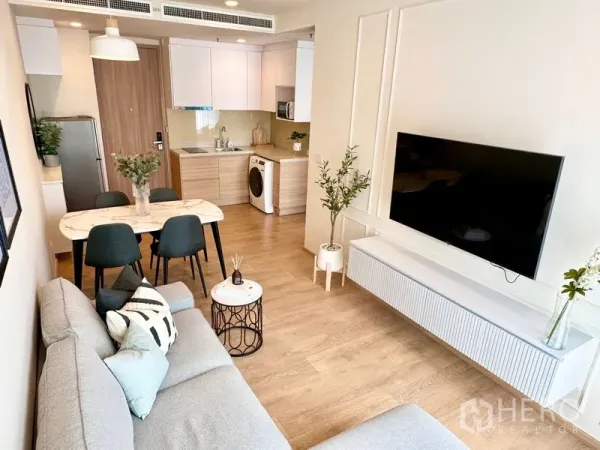 公寓 出租在Watthana, Bangkok - 开放式客餐厨空间，浅色木地板与绿植，墙挂电视。