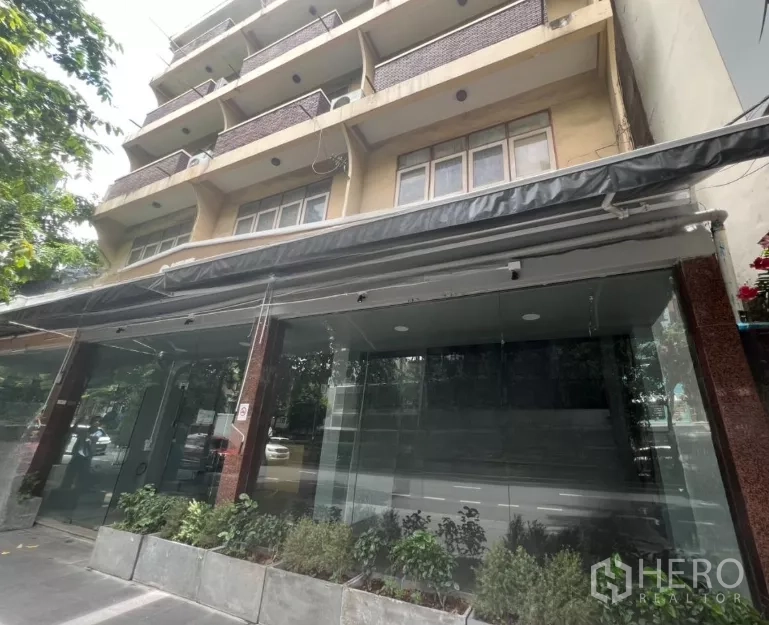 อาคารพาณิชย์ ให้เช่าในWatthana, Bangkok - ด้านหน้าอาคารหลายชั้นพร้อมกระจกเต็มหน้ากว้างและแปลงต้นไม้ด้านล่าง.