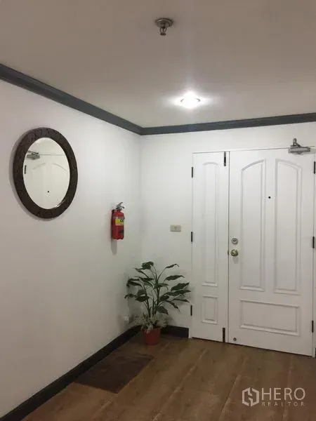 Condominium for rent in Watthana, Bangkok - Condo entry foyer with white paneled door, round mirror, potted plant and wood flooring.