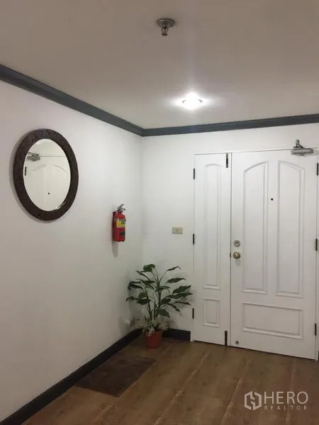 Condominium for rent in Watthana, Bangkok - Condo entry foyer with white paneled door, round mirror, potted plant and wood flooring.