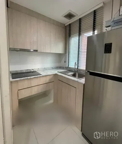 ทาวน์เฮาส์ ขายในSuan Luang, Bangkok - ครัวรูปตัวแอล ตู้ลายไม้ เคาน์เตอร์ลายหิน และตู้เย็นสแตนเลสใกล้หน้าต่าง