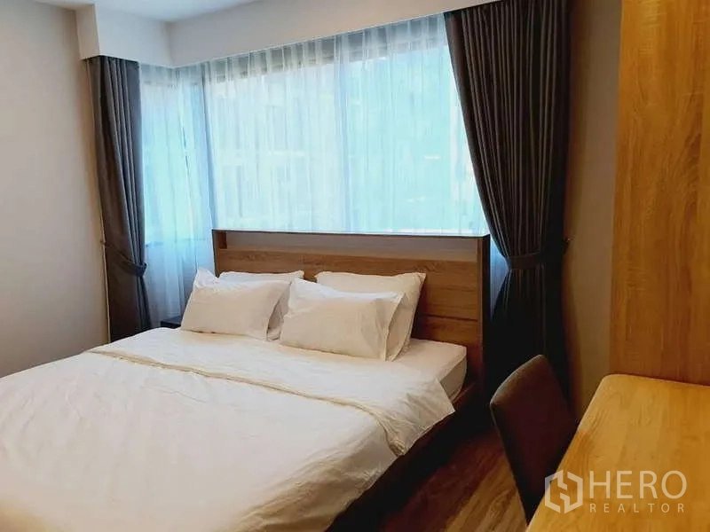 Condominium for rent in Sathon, Bangkok - Corner bedroom with large windows, double bed and full-length curtains.