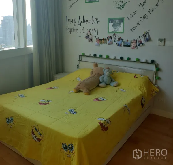 คอนโด ขายในKhlong Toei, Bangkok - ห้องนอนอบอุ่นมีหน้าต่างวิวเมือง ผนังตกแต่งข้อความ และเตียงควีนผ้าปูสีเหลือง