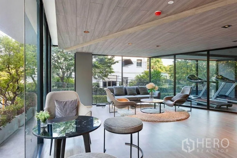 Condominium for rent or sale in Watthana, Bangkok - Resident lounge with modern sofas, round tables and glass walls offering garden views next to the gym.