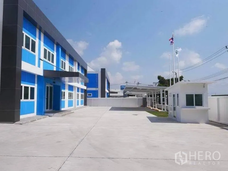 工厂 出租在Bang Bo, Samut Prakan - 厂区宽敞车道与停车区，设有门卫室与旗杆，蓝灰色办公楼立面与围墙