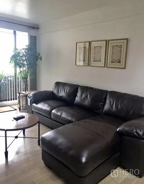 คอนโด ให้เช่าในKhlong Toei, Bangkok - ห้องนั่งเล่นโซฟาหนังสีเข้ม โต๊ะกลางทรงกลม และประตูกระจกบานเลื่อนออกสู่ระเบียง