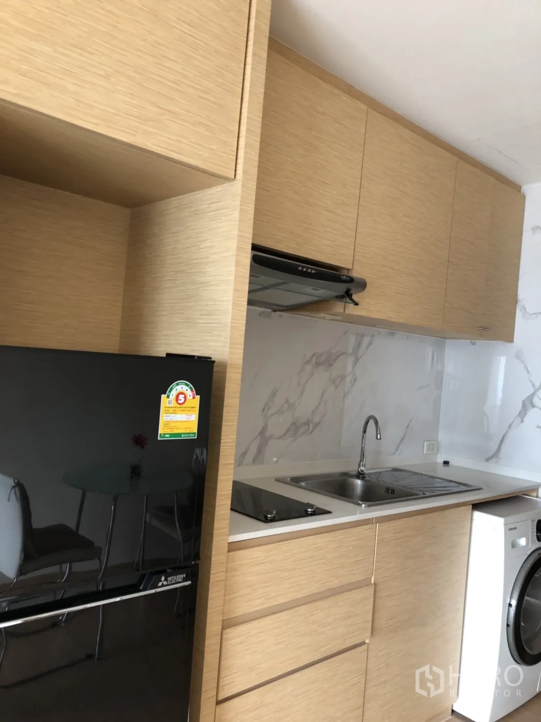 公寓 出租在Khlong Toei, Bangkok - 一字型开放式厨房，木质橱柜、洗槽、灶台、油烟机、黑色冰箱与洗衣机齐全。
