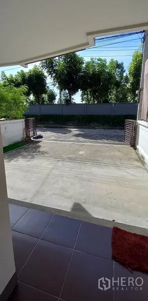 ทาวน์เฮาส์ ขายในMueang Pathum Thani, Pathum Thani - ที่จอดรถหน้าบ้านและลานคอนกรีตกว้าง พร้อมประตูรั้วเลื่อนและต้นไม้ด้านหน้า