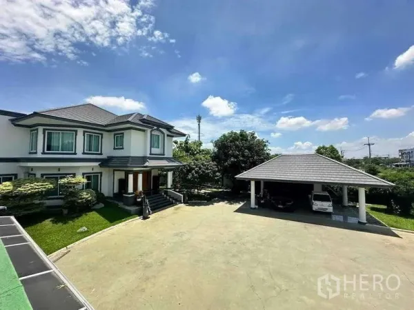 บ้าน ขายในKhlong Luang, Pathum Thani - ลานจอดรถขนาดใหญ่พร้อมบ้านสองชั้นและโรงจอดรถมีหลังคา ท่ามกลางสนามหญ้า