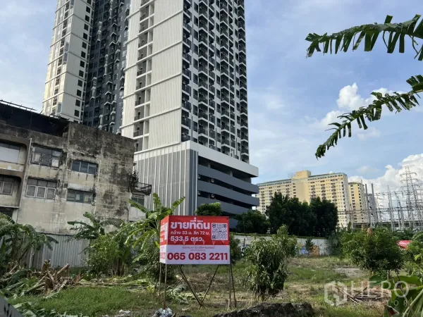 ที่ดิน ขายในSuan Luang, Bangkok - ภาพระดับถนนเห็นที่ดินพร้อมป้ายขาย ข้างคอนโดมิเนียมสูง