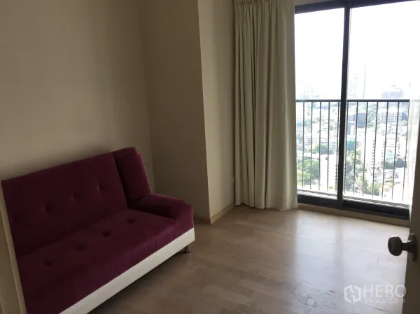 Condominium for rent in Khlong Toei, Bangkok - Bright room with purple sofa and sliding doors to a balcony with Bangkok skyline view.