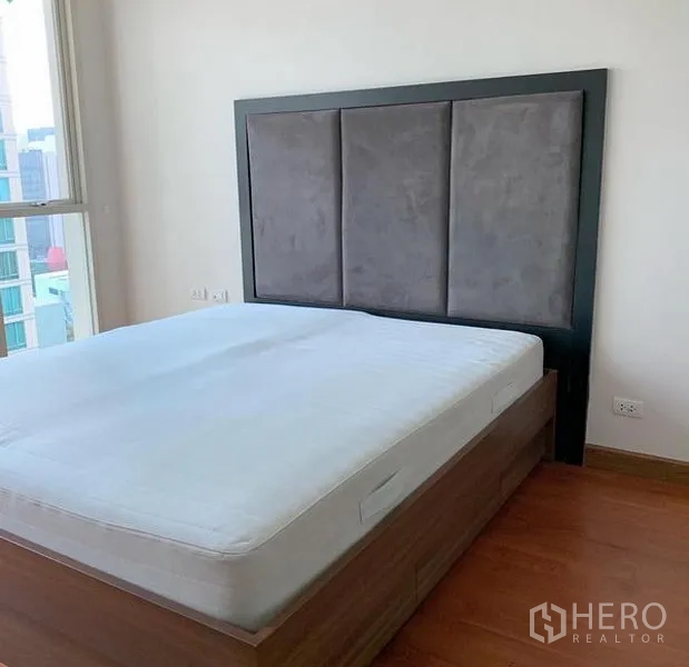 คอนโด ให้เช่าในPathum Wan, Bangkok - ห้องนอนพร้อมหัวเตียงบุผ้า หน้าต่างวิวเมือง และพื้นไม้โทนอุ่น ในคอนโดปทุมวัน